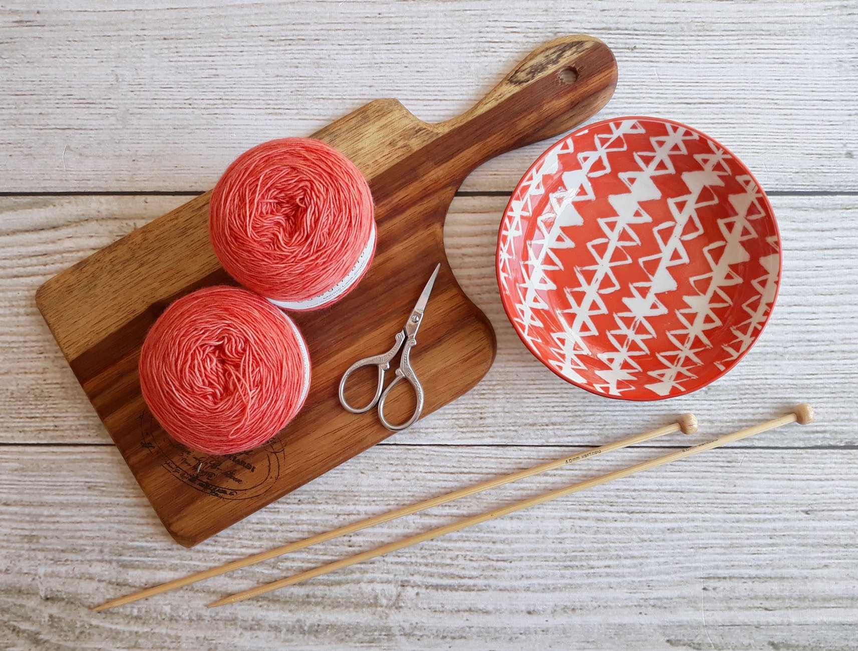 two pink spools on brown wooden chopping board beside orange bowl